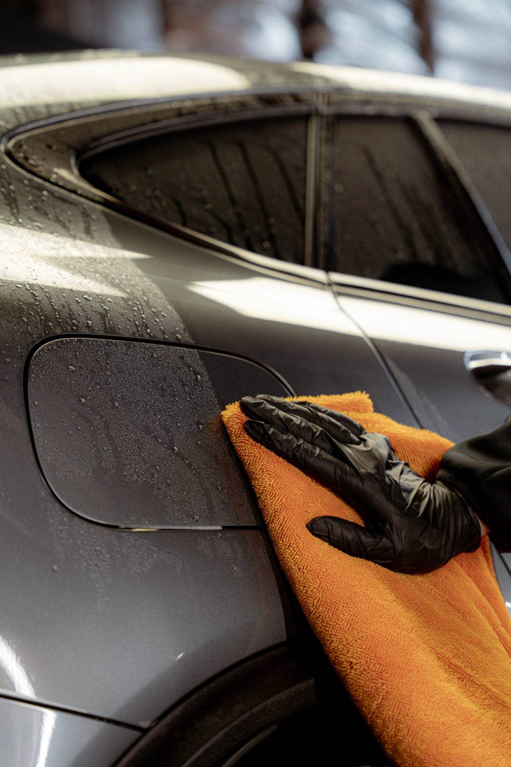 Gloved hand drying a car panel with the orange WORK STUFF MONSTER drying towel
