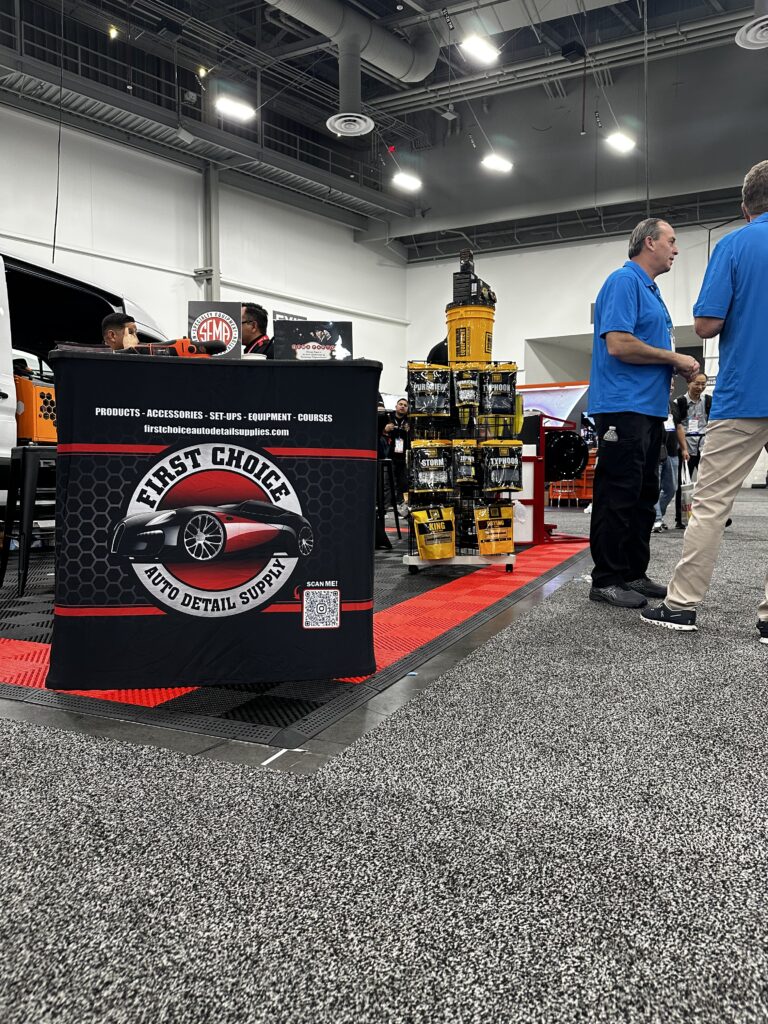 First Choice Auto Detail Supply booth at SEMA Show 2025 with blue-shirted people and shelves of detailing products.
