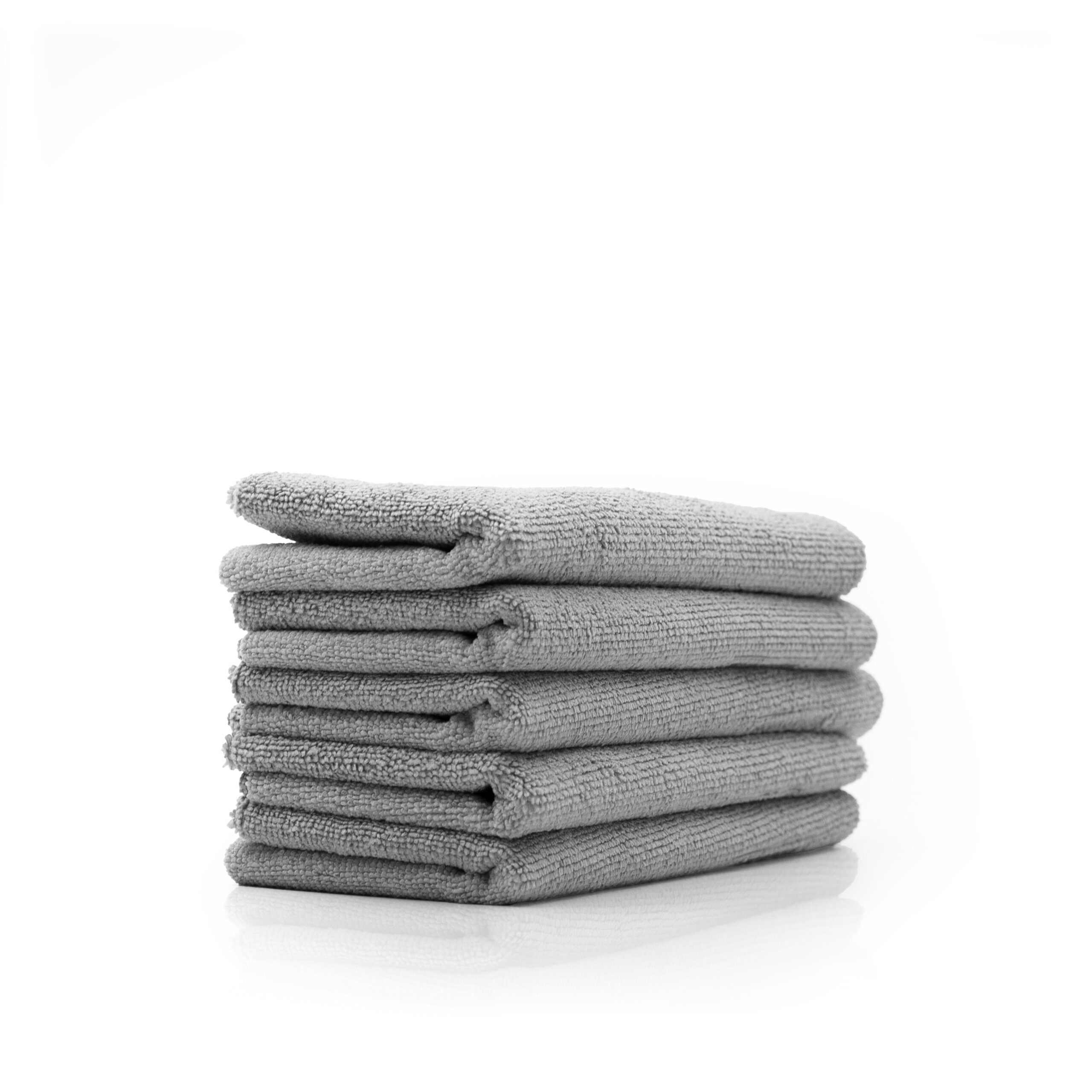 Cinq serviettes grises soigneusement empilées sur une surface blanche, avec un reflet subtil en dessous.