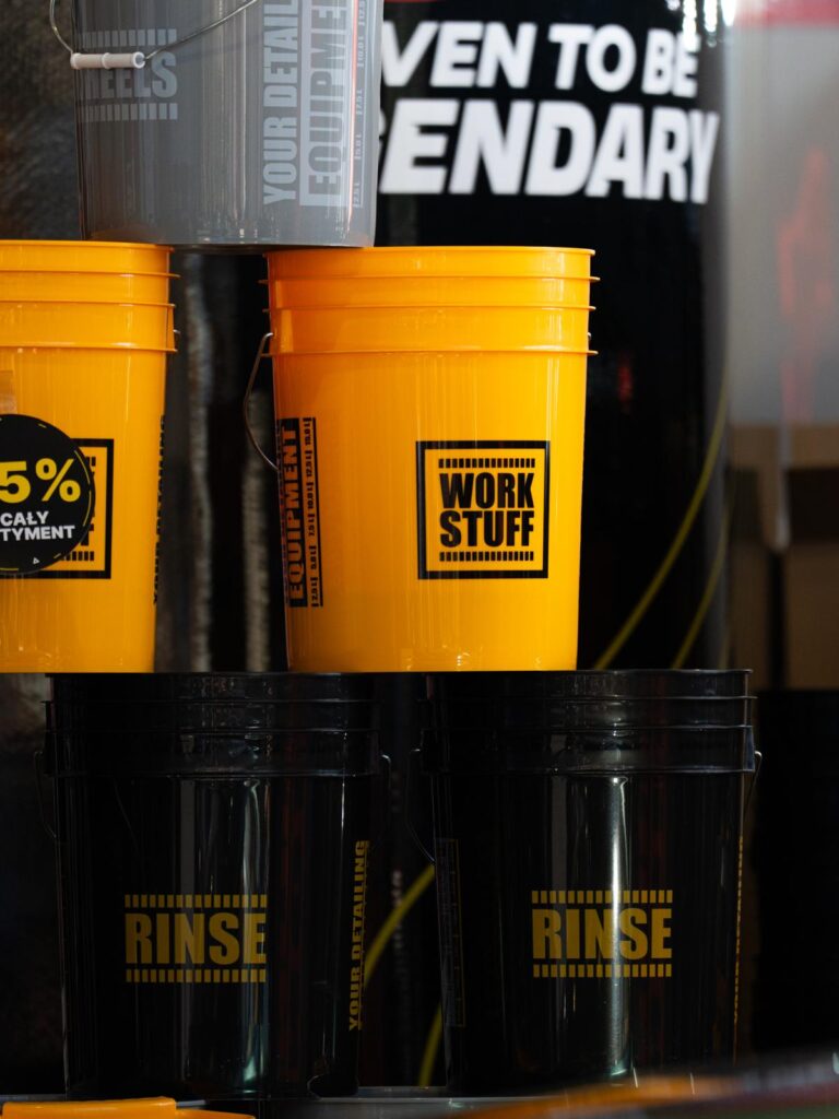 Stacked orange and black Work Stuff buckets labeled WORK STUFF and RINSE, with a gray bucket and a sign in the background. Stacked orange and black Work Stuff buckets labeled WORK STUFF and RINSE, with a gray bucket and a sign in the background.